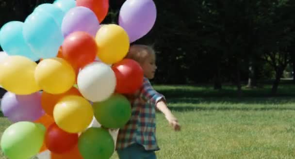 Portret meisje spinnen met ballonnen in de weide op camera en zwaaien hand op camera — Stockvideo