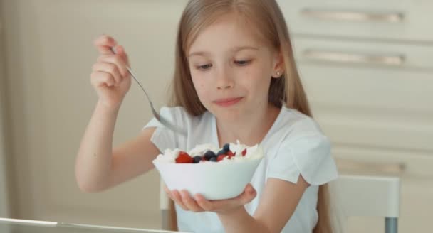 Menina comendo um morango de um prato e sorrindo para a câmera — Vídeo de Stock