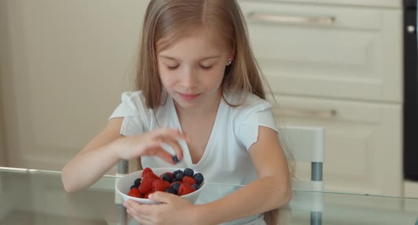 Dívka jíst borůvky z talíře a usmívá se na kameru — Stock video