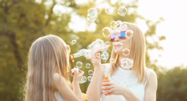 Laughing family blowing bubbles face to face in the sunlight at sunset in the park — Stock Video