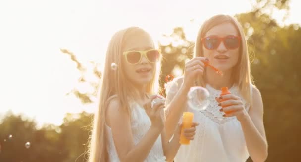 Skrattande familj blåser bubblor i solljus vid solnedgången i parken — Stockvideo