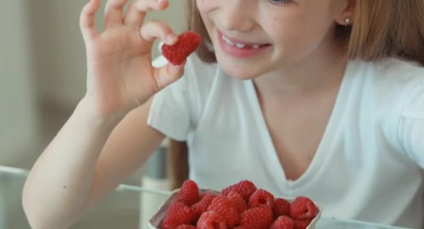 Retrato de close-up de menina que comer uma framboesa e sorrindo para a câmera. Polegar para cima. Está bem. — Vídeo de Stock