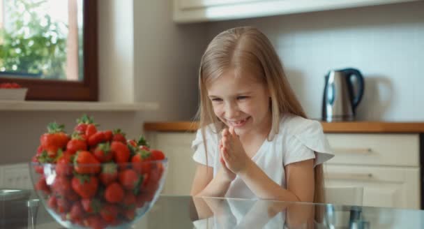 El niño se frota las manos. Chica admirando un gran plato de fresas y mirando a la cámara y abrazándola — Vídeos de Stock