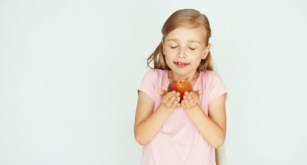 Fille reniflant et tenant pêche et souriant à la caméra. Enfant avec des fruits sur fond blanc — Video