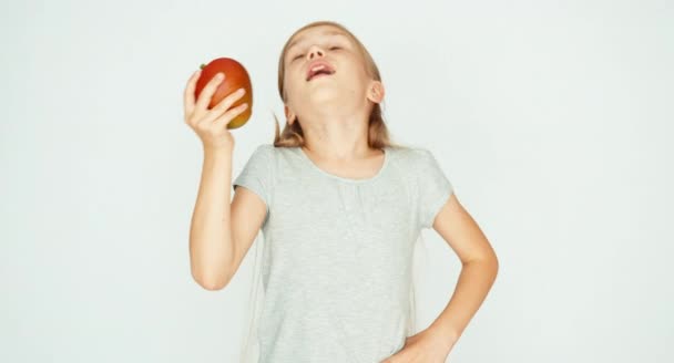 Chica oliendo un mango y riéndose de la cámara. Niño con fruta sobre fondo blanco — Vídeos de Stock