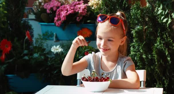 Ragazza che mangia una ciliegia. Bambino mangiare bacche e li ammira e guardando la fotocamera e agitando la mano. Pollice in alto. Va bene. — Video Stock