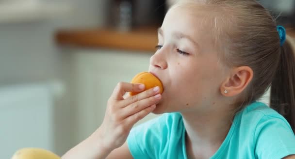 Extrem närbild porträtt flicka äter aprikos. Barnet sitter i köksbordet. Tummen upp. Okej — Stockvideo