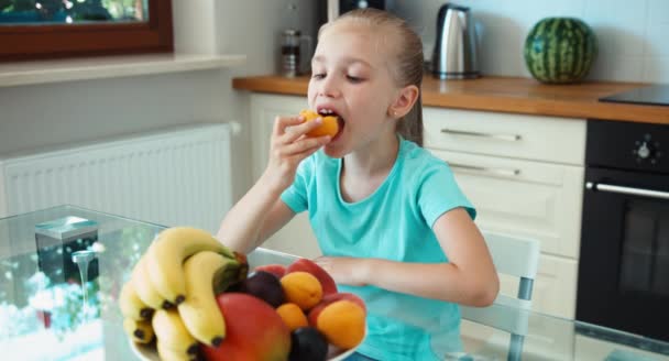 Девушка ест абрикос. Ребенок сидит на кухонном столе. Пальцем вверх. Хорошо. — стоковое видео