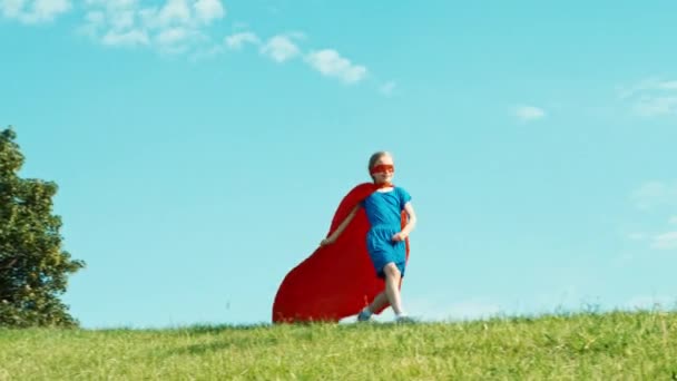 Boldog szuperhős lány gyermek 7-8 éves futás és spinning ellen a kék ég — Stock videók