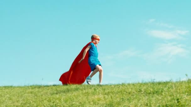 Gelukkig superheld meisje 7-8 jaar oud lopen tegen de blauwe hemel — Stockvideo