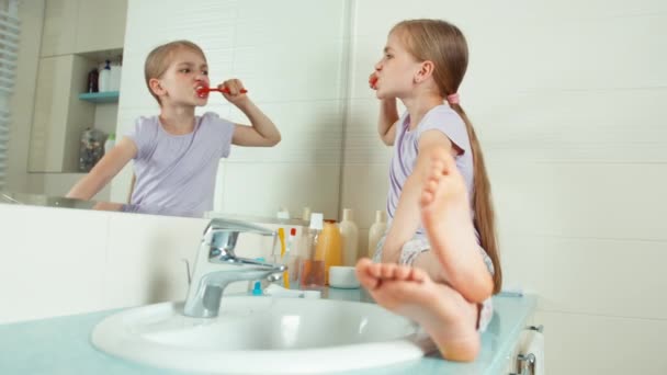 Портрет девушки с помощью зубной щетки и чистки зубов. Девушка смотрит на свои зубы, сидя у зеркала в ванной комнате — стоковое видео