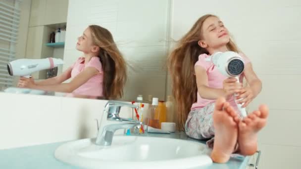 7-8 éves lány szárad egy hajszárító a fürdőszobában, mosolygó, a kamera hosszú gyönyörű haját — Stock videók