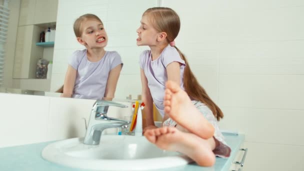 Portrét roztomilá dívka sedí u zrcadla v koupelně a zobrazení její zuby a pomocí kartáčku — Stock video