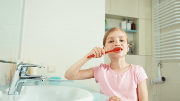 Портрет дівчинки-дитини 7-8 років прибирання зубів у ванній кімнаті і погляд на камеру. Палець вгору. гаразд — стокове відео