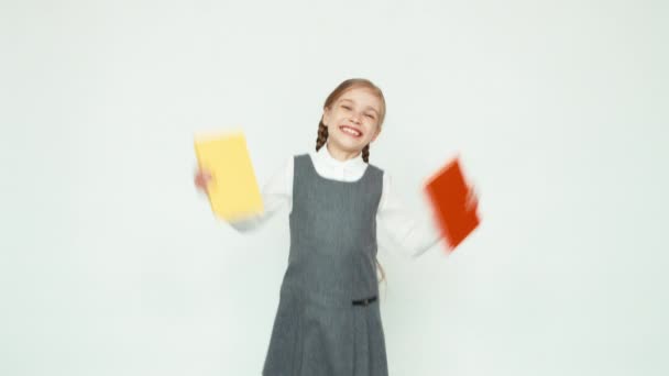 Att studera är över. Lycklig Skolflicka 7-8 år hålla böcker och hoppa med böcker på vit bakgrund och ler mot kameran med tänder. Upp med händerna. Okej — Stockvideo