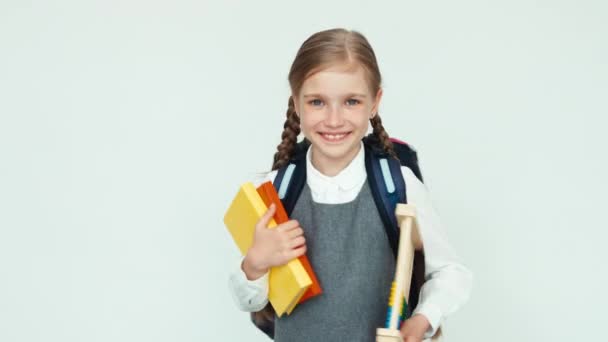 Portret schattig schoolmeisje kind 7-8 jaar met rugzak holding abacus en boeken op witte achtergrond glimlachend met tanden op camera — Stockvideo