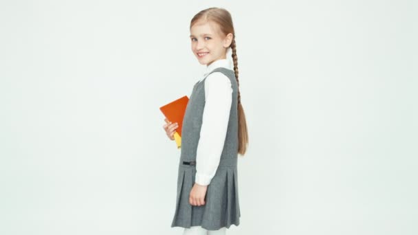 Schattig schoolmeisje 7-8 jaar houden boeken draait zich om op camera op witte achtergrond en glimlachend op camera met tanden. Duim omhoog. OK — Stockvideo