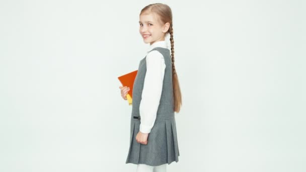 Portret schoolmeisje 7-8 jaar houden boeken draait zich om op camera op witte achtergrond en glimlachend op camera met tanden — Stockvideo
