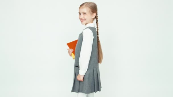 Colegiala retrato 7-8 años sosteniendo libros se da la vuelta en la cámara sobre fondo blanco y sonriendo a la cámara con los dientes — Vídeos de Stock