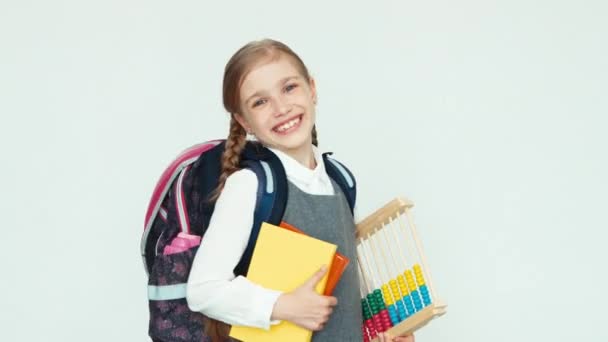 Ritratto carino studentessa bambino 7-8 anni con zaino in mano abaco e libri su sfondo bianco ridere con i denti alla macchina fotografica — Video Stock