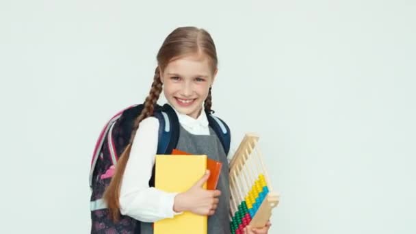 Портрет милої школярки 7-8 років з рюкзаком, який тримає живіт і книги на білому тлі, сміючись зубами — стокове відео