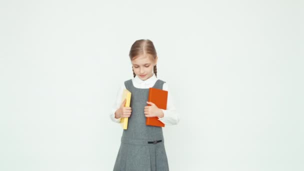 Lo studio è finito. Carino scuola ragazza 7-8 anni in possesso di libri e saltare con libri su sfondo bianco e sorridente alla fotocamera con i denti. Mani in alto. Va bene. — Video Stock