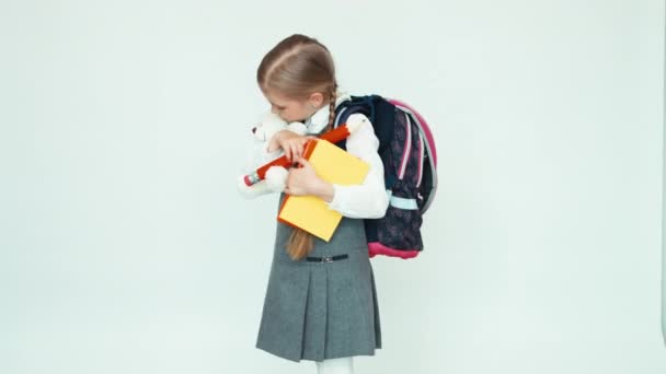 Милая школьница 7-8 лет разговаривает с плюшевым мишкой. Ребенок держит книги и большой карандаш и улыбается в камеру на белом фоне — стоковое видео