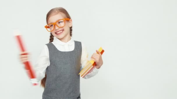 Schoolmeisje kind 7-8 jaar glimlachend in de camera. Meisje met bril holding boeken en een grote potlood. — Stockvideo