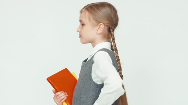 Porträtt Söt skolflicka 7-8 år hålla böcker på vit bakgrund och ler med tänder på kamera — Stockvideo