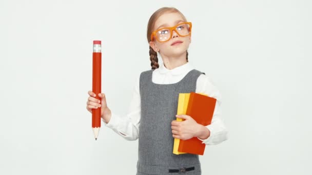 Colegiala niño de 7-8 años con gafas sosteniendo libros y un lápiz grande. Aislado sobre fondo blanco — Vídeos de Stock