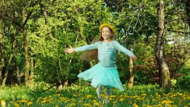Крутящаяся девочка 7-8 лет с венком из одуванчиков на голове, кружащейся в парке и улыбающейся солнцу — стоковое видео