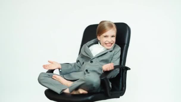 Business tjej 7-8 år gammal i en verksamhet passar sitter på stolen på vit bakgrund spinning — Stockvideo