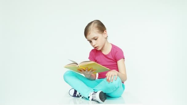 かわいい女の子 7-8 年の本を読んで、白い背景で笑いながら — ストック動画