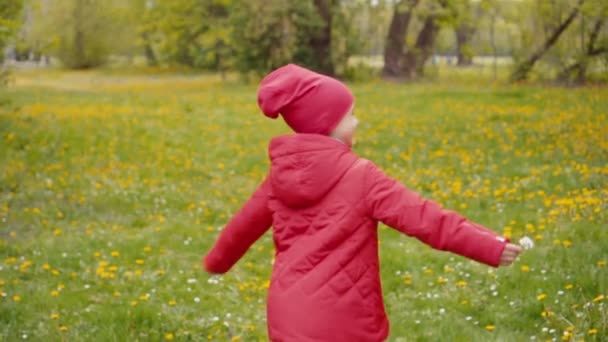 7-8-летняя девушка в красной куртке и шляпе, крутящаяся в парке весной. Медленное движение от Sony A6300 — стоковое видео