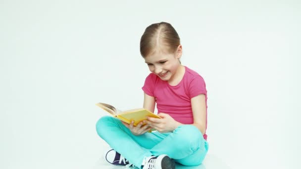 Menina bonito 7-8 anos abraçando livro no fundo branco e sorrindo para a câmera — Vídeo de Stock