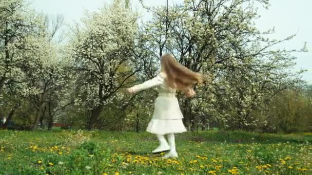 Girl child 7-8 years old in coat spinning against the backdrop of flowering trees — Stock video