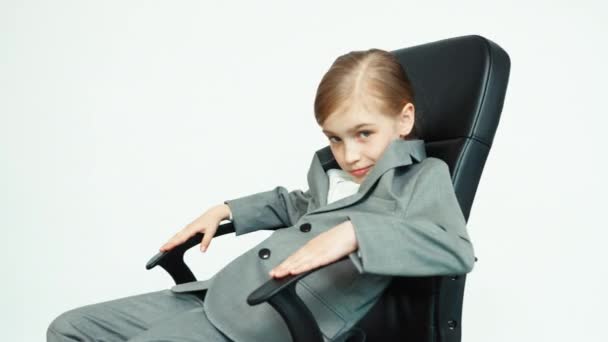 Business girl 7-8 years old in a business suit on white background sitting on the chair — Stockvideo