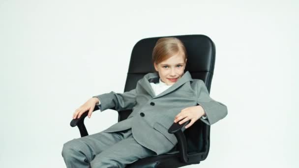 Business girl 7-8 years old in a business suit sitting on the chair on white background — Stockvideo