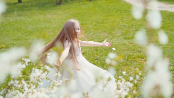 Chica rubia feliz 7-8 años de edad, girando en un vestido blanco en la hierba. Sony A6300 de cámara lenta — Vídeos de Stock