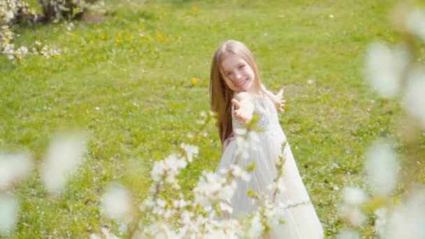 Chica rubia feliz 7-8 años de edad, girando en un vestido blanco en la hierba en la nieve de primavera. Sony A6300 de cámara lenta — Vídeo de stock