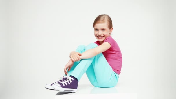 Happy girl 7-8 years looking and smiling at camera. Child sitting on the white background — Stockvideo