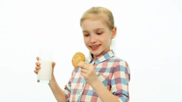 Dziewczyna, picie mleka i jedzenia ciasteczko i uśmiecha się do kamery na białym tle — Wideo stockowe
