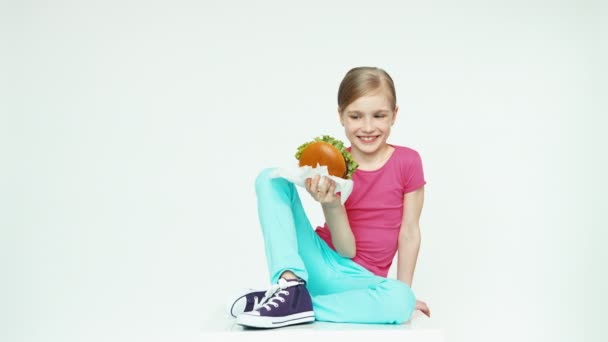 Meisje 7-8 jaar mooie bedrijf hamburger. Duim omhoog. OK — Stockvideo