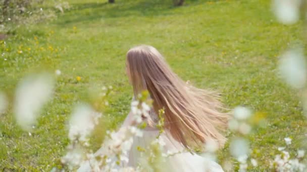 Super neve primavera. Menina loira feliz 7-8 anos de idade girando em um vestido branco na grama na neve primavera. Movimento lento Sony A6300 — Vídeo de Stock