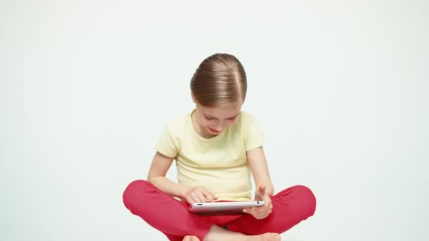 Девочка 7-8 лет на планшетном компьютере, сидящая на белом фоне — стоковое видео