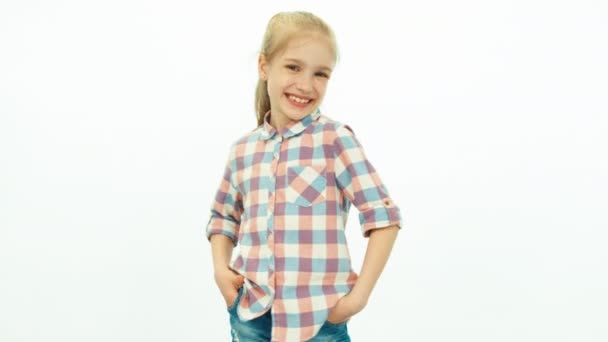 7-8 years old girl in the jeans and a shirt standing on the white background and smiling at camera — Stock video