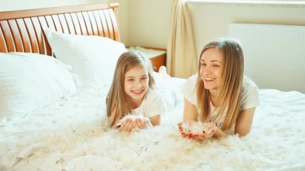 Süße Mädchen liegen auf dem Bett und spielen mit Flaum und Federn — Stockvideo