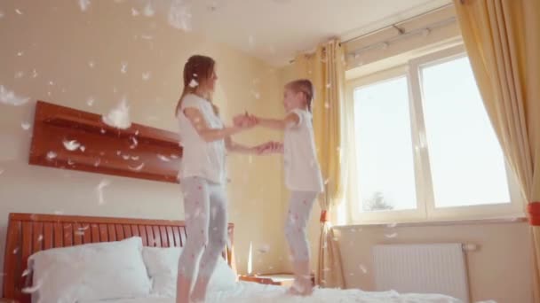 Happy daughter and mother jumping and spinning on the bed. Among the fluff and feathers. Slowmotion — ストック動画