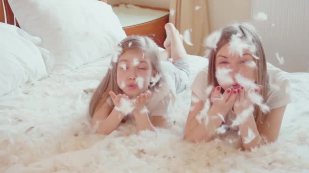 Meninas bonitos felizes deitado na cama e brincando com fluff e penas. Movimento lento — Vídeo de Stock