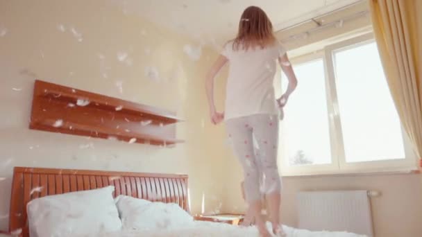 Nette Mädchen springen und drehen sich auf dem Bett. zwischen Flaum und Federn. Zeitlupe — Stockvideo